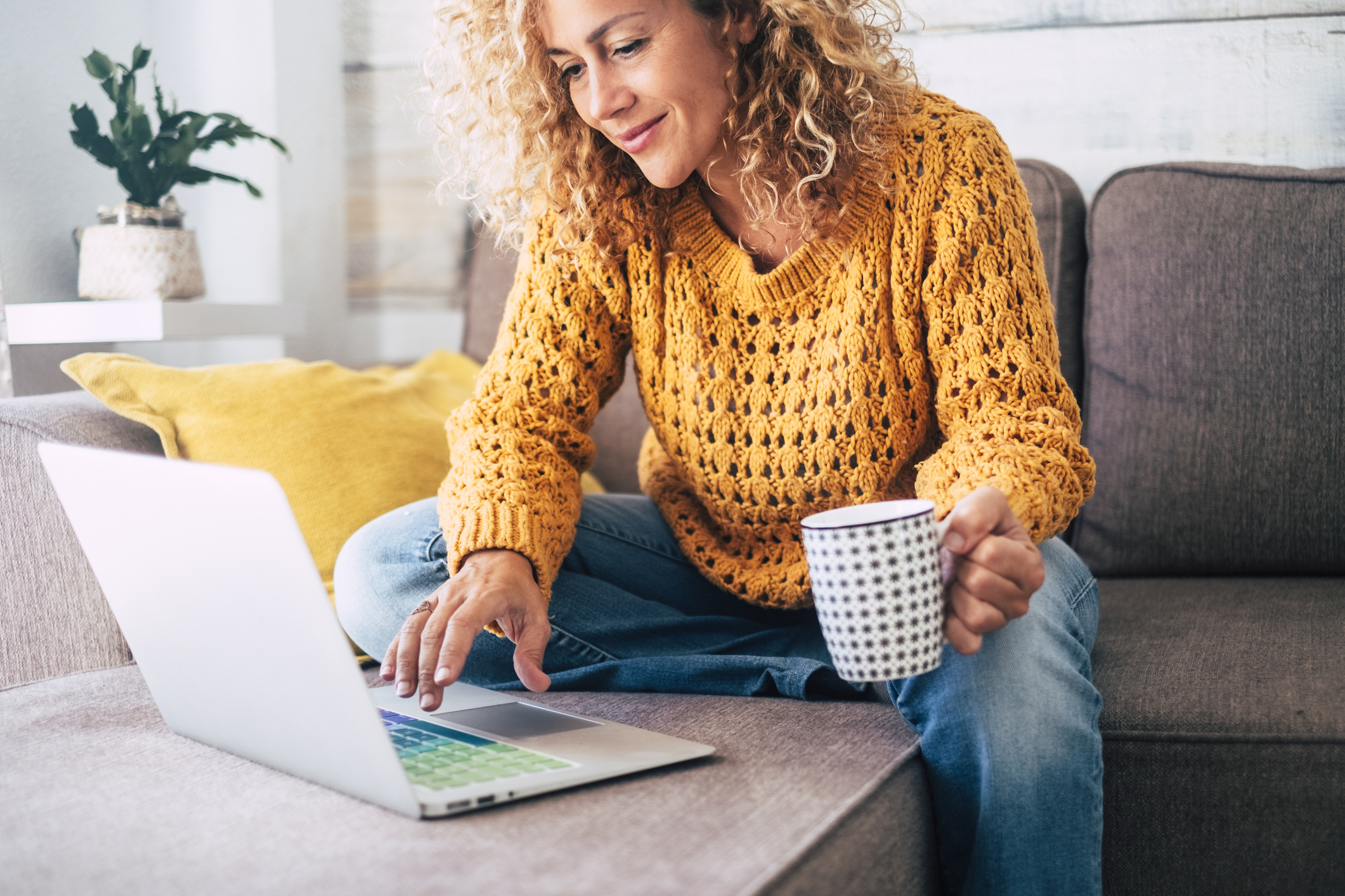 woman sitting on her couch working on her laptop while drinking coffee