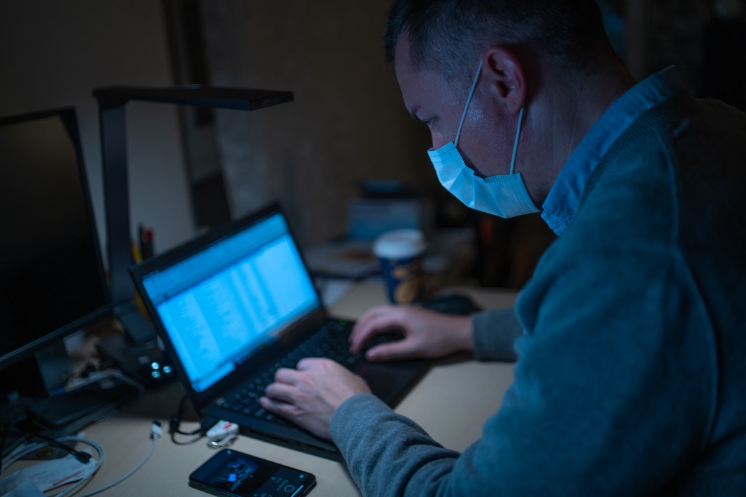 man wearing mask working at desk on laptop